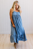 Woman wearing a blue denim dress standing against a white wall.
