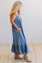 Woman wearing a blue dress with ruffled layers on a light wooden floor.