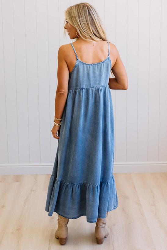 Woman wearing a blue denim dress standing against a white wall.