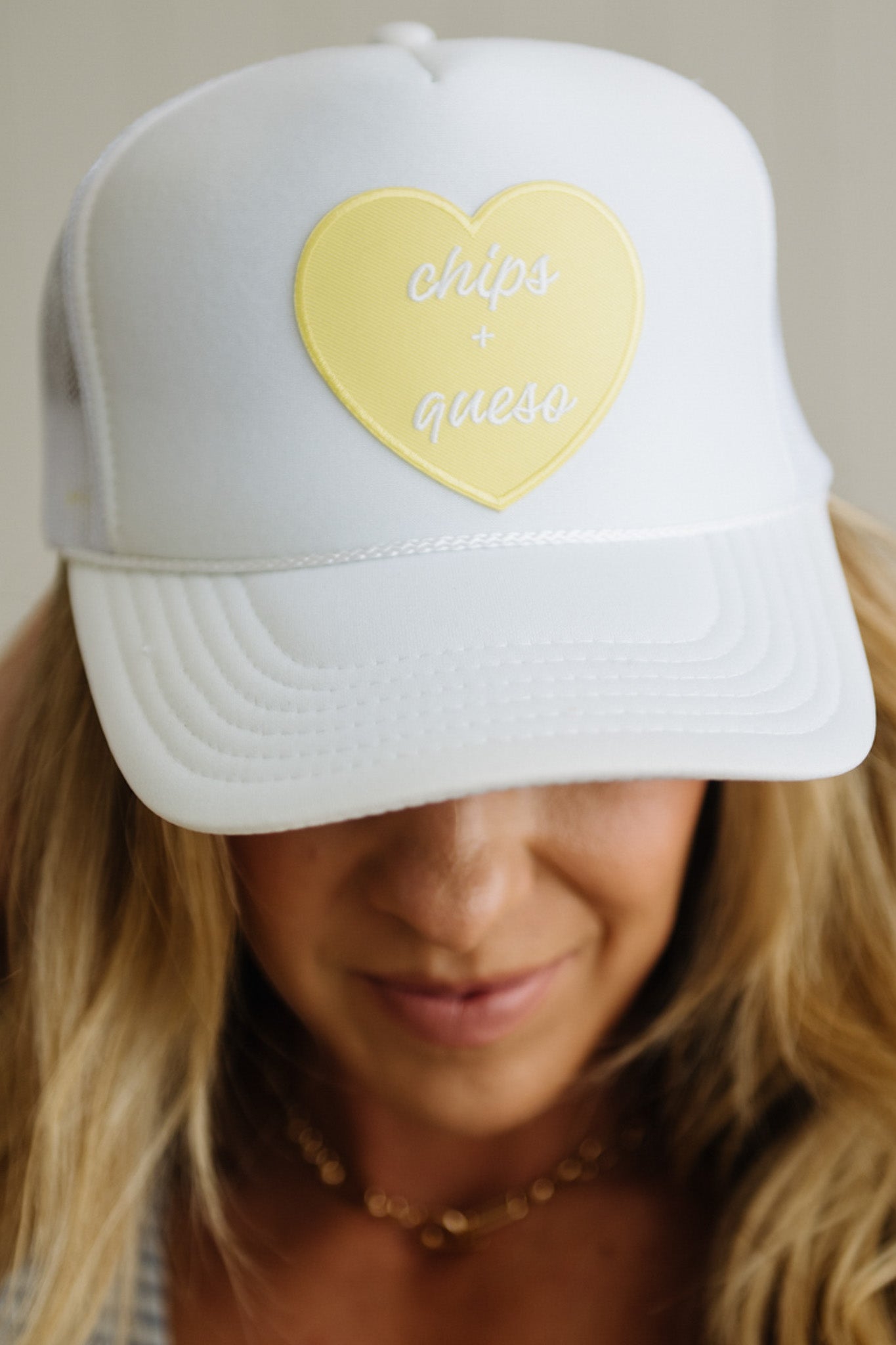 White cap with a yellow heart-shaped patch and 'chips & queso' text on a neutral background