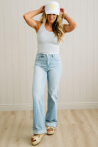Woman wearing a white tank top, light blue jeans, and a white cap with a yellow heart design.