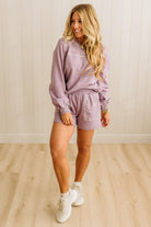 Woman wearing a lavender loungewear set with white sneakers in a room with wooden flooring and white walls.