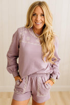 Woman wearing a matching lavender outfit with embroidered details on a plain background