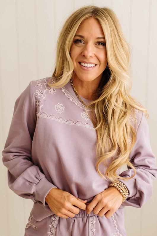 Woman wearing a light purple dress with lace details against a plain background
