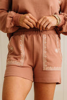 Person wearing a matching brown sweatshirt and shorts set with white embroidery on a neutral background