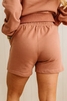 Person wearing a brown sweatshirt and shorts set against a neutral background