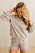 Woman wearing a light gray sweatshirt and shorts set with lace details against a plain background
