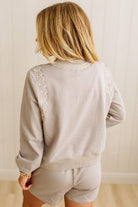 Person wearing a light gray outfit with lace details on a plain background