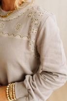 Light gray sweater with intricate lace detailing on a neutral background