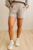Person wearing light gray shorts with lace details on a wooden floor.