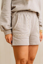 Light gray shorts with white embroidery on a neutral background