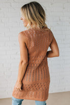 Woman wearing a brown knitted vest against a white brick wall.