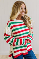 BLONDE WOMAN IN DARK JEANS STANDING IN A BRIGHTLY LIT STUDIO AND WEARING A CHRISTMAS CANDY STRIPE COZY KNIT PULLOVER IN CREAM GREEN AND RED.