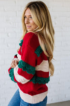 BLONDE WOMAN WEARING A CHRISTMAS THEME RUFFLED DETAILS SWEATER TOP IN RED, CREAM, AND HUNTER GREEN.