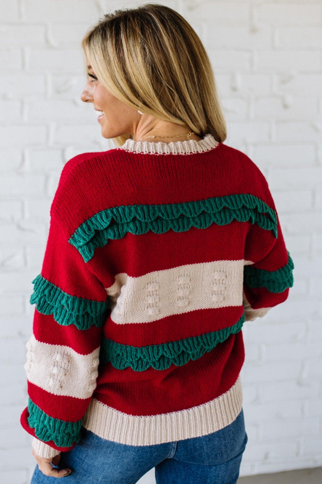 BLONDE WOMAN WEARING A CHRISTMAS THEME RUFFLED DETAILS SWEATER TOP IN RED, CREAM, AND HUNTER GREEN.