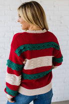 BLONDE WOMAN WEARING A CHRISTMAS THEME RUFFLED DETAILS SWEATER TOP IN RED, CREAM, AND HUNTER GREEN.