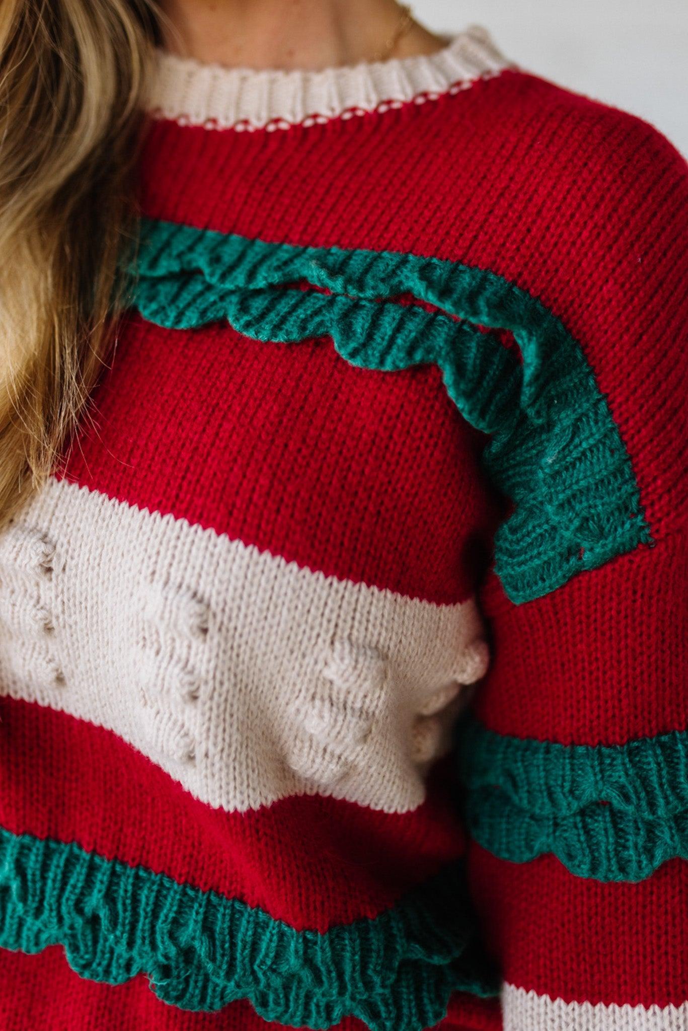 BLONDE WOMAN WEARING A CHRISTMAS THEME RUFFLED DETAILS SWEATER TOP IN RED, CREAM, AND HUNTER GREEN.