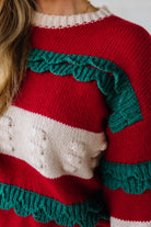 BLONDE WOMAN WEARING A CHRISTMAS THEME RUFFLED DETAILS SWEATER TOP IN RED, CREAM, AND HUNTER GREEN.