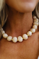 A close-up of a woman wearing a chunky beaded necklace made of cream-colored stone beads with small gold spacer rings.