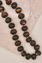 A beaded necklace with glossy dark brown and black marbled beads separated by small gold spacer beads, displayed on a light textured surface.