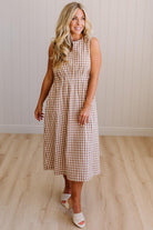Woman wearing a checkered dress standing in a room with wooden flooring and a white paneled wall.