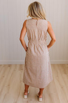 Woman wearing a checkered dress standing against a plain wall.