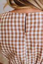 Woman wearing a checkered dress standing against a plain wall.