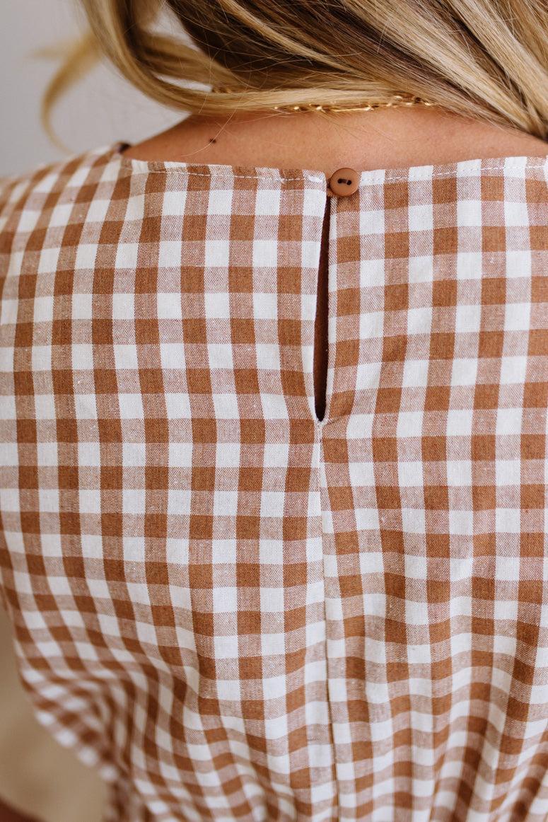 Woman wearing a checkered dress standing against a plain wall.