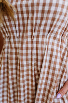Woman wearing a checkered dress standing against a plain wall.