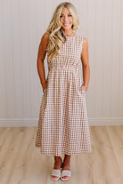Woman wearing a checkered dress standing against a plain wall.