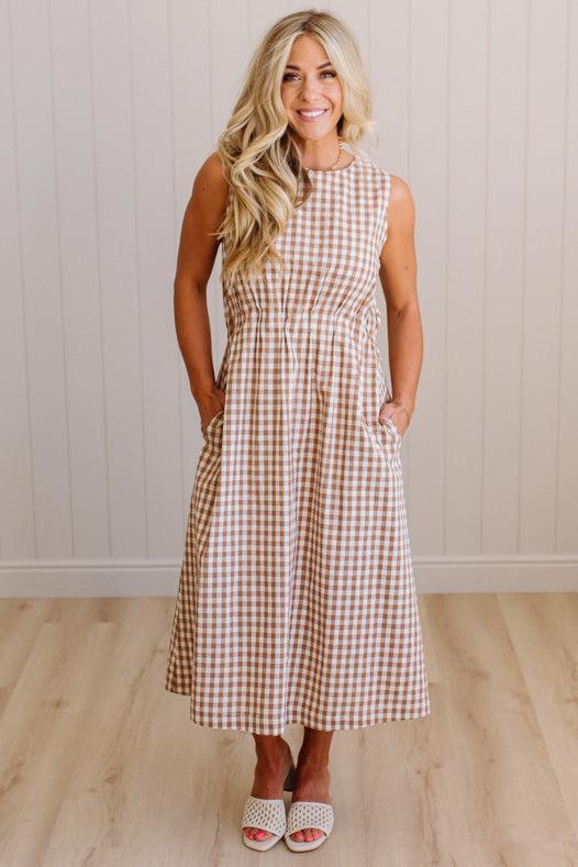 Woman wearing a checkered dress standing against a plain wall.