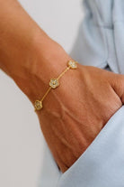 Gold bracelet with floral designs on a wrist against a light background