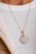 A close-up of a delicate gold chain necklace with a polished, irregularly shaped pale pink stone pendant, worn on a person's neck over a white ribbed top.