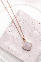 Rose gold necklace with a polished, irregular-shaped pale pink stone pendant, displayed on a textured light pink stone tile over a white plate.