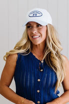 Woman wearing a white cap with a logo and a blue sleeveless top, standing against a light background.
