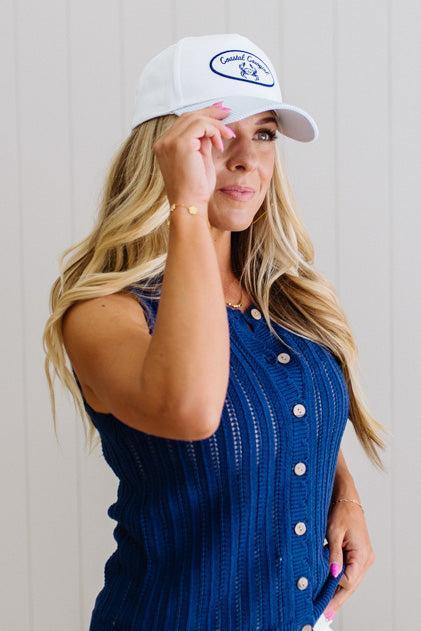 Woman wearing a blue sleeveless top and white cap with branding, against a plain background