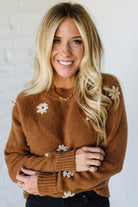 Woman wearing a brown sweater with floral embellishments against a white background