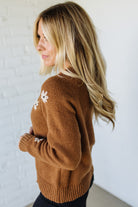 Woman wearing a brown sweater with floral details against a white background