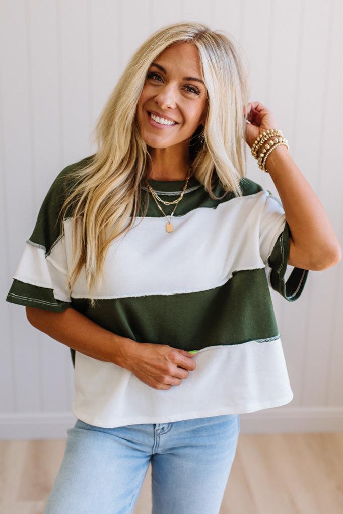 Woman wearing a green and white striped shirt with light blue jeans against a plain background