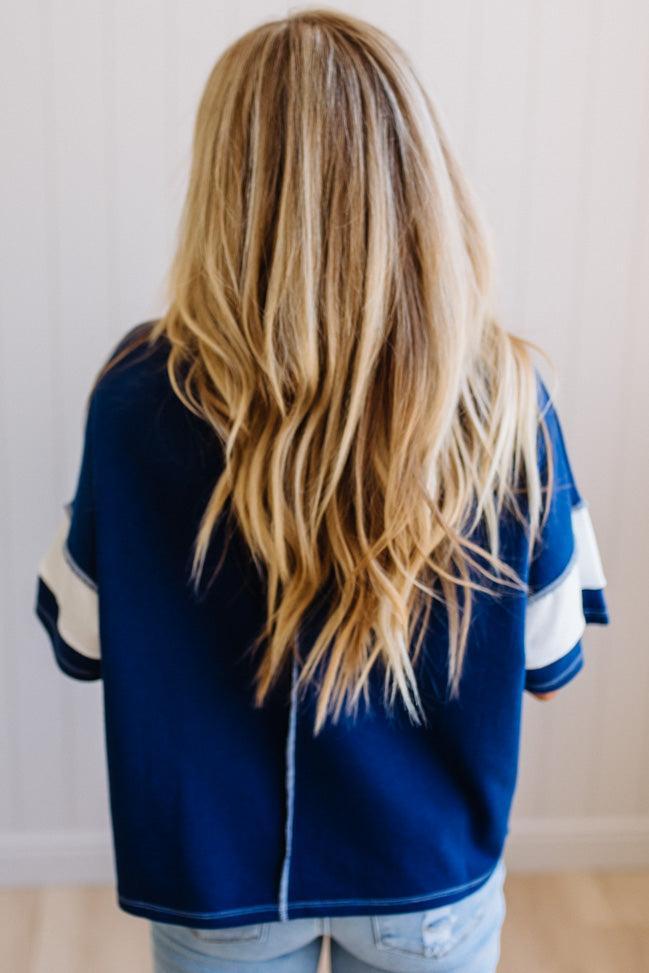 Person wearing a blue varsity jacket with white stripes from behind