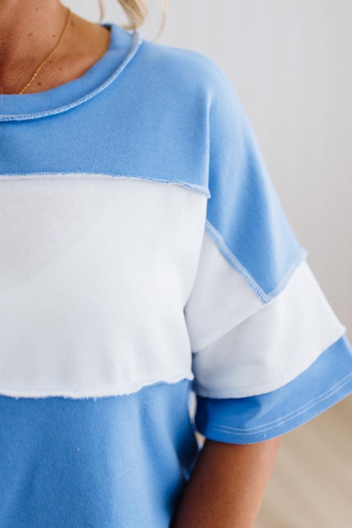 Person wearing a blue oversized shirt with white sleeves against a light background