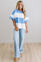 Woman wearing a blue and white striped sweater and light blue jeans indoors.
