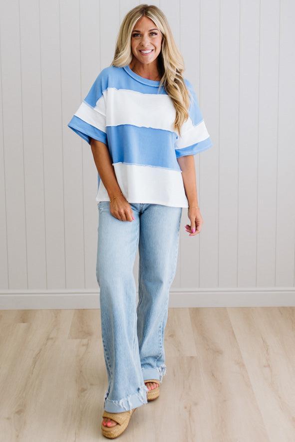 Woman wearing a blue and white striped sweater and light blue jeans indoors.