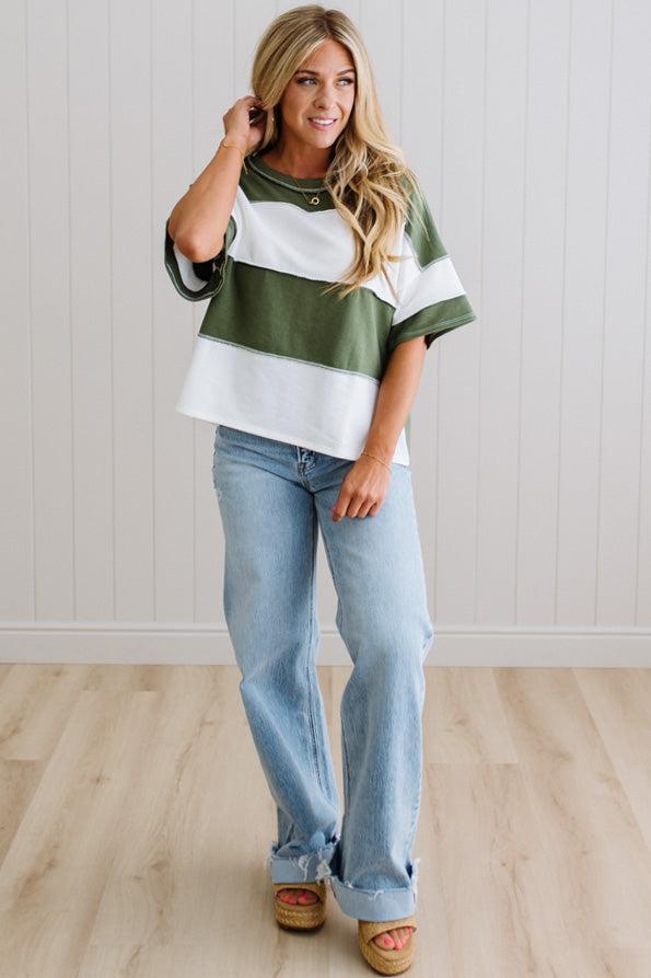 Woman wearing a striped shirt and jeans standing in a room with a light wooden floor and white walls.