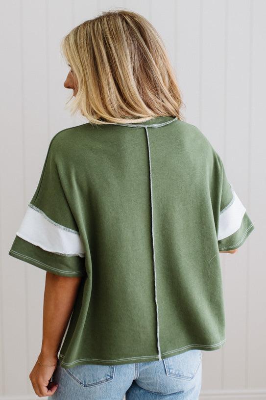 Person wearing a green oversized shirt with white sleeves against a light background


