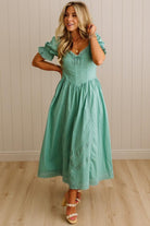 Woman wearing a teal dress with ruffled sleeves against a beige wall.