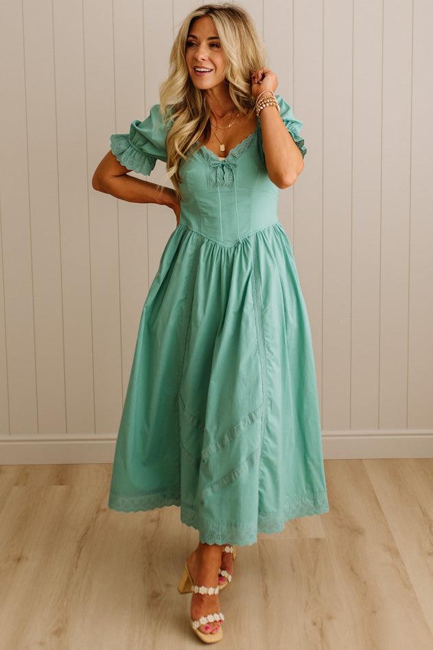 Woman wearing a teal dress with ruffled sleeves against a beige wall.