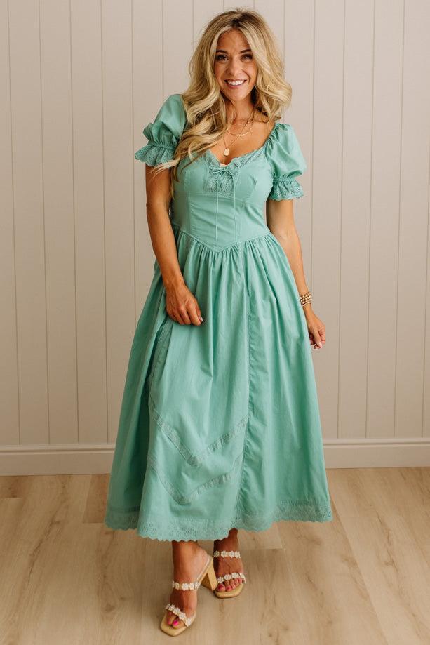Woman wearing a green dress standing against a beige wall.