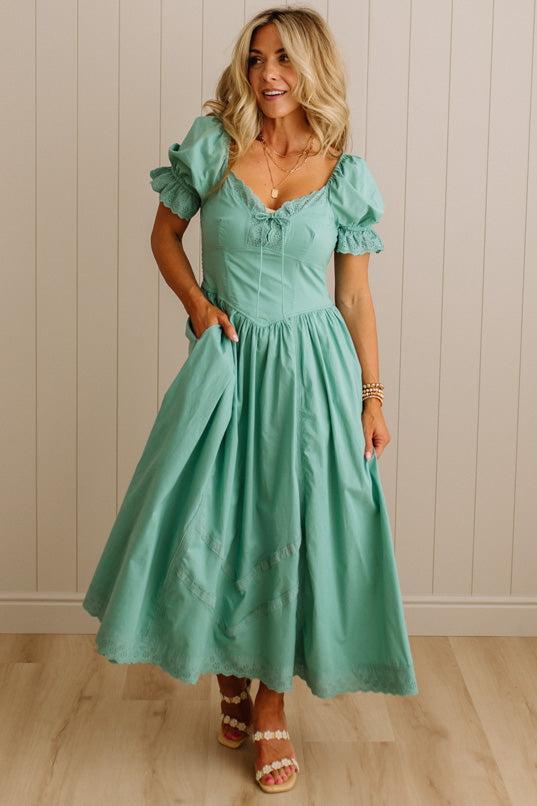 Woman wearing a teal dress with ruffled sleeves against a neutral background