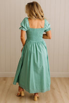 Woman wearing a green dress with ruffled sleeves against a beige wall.